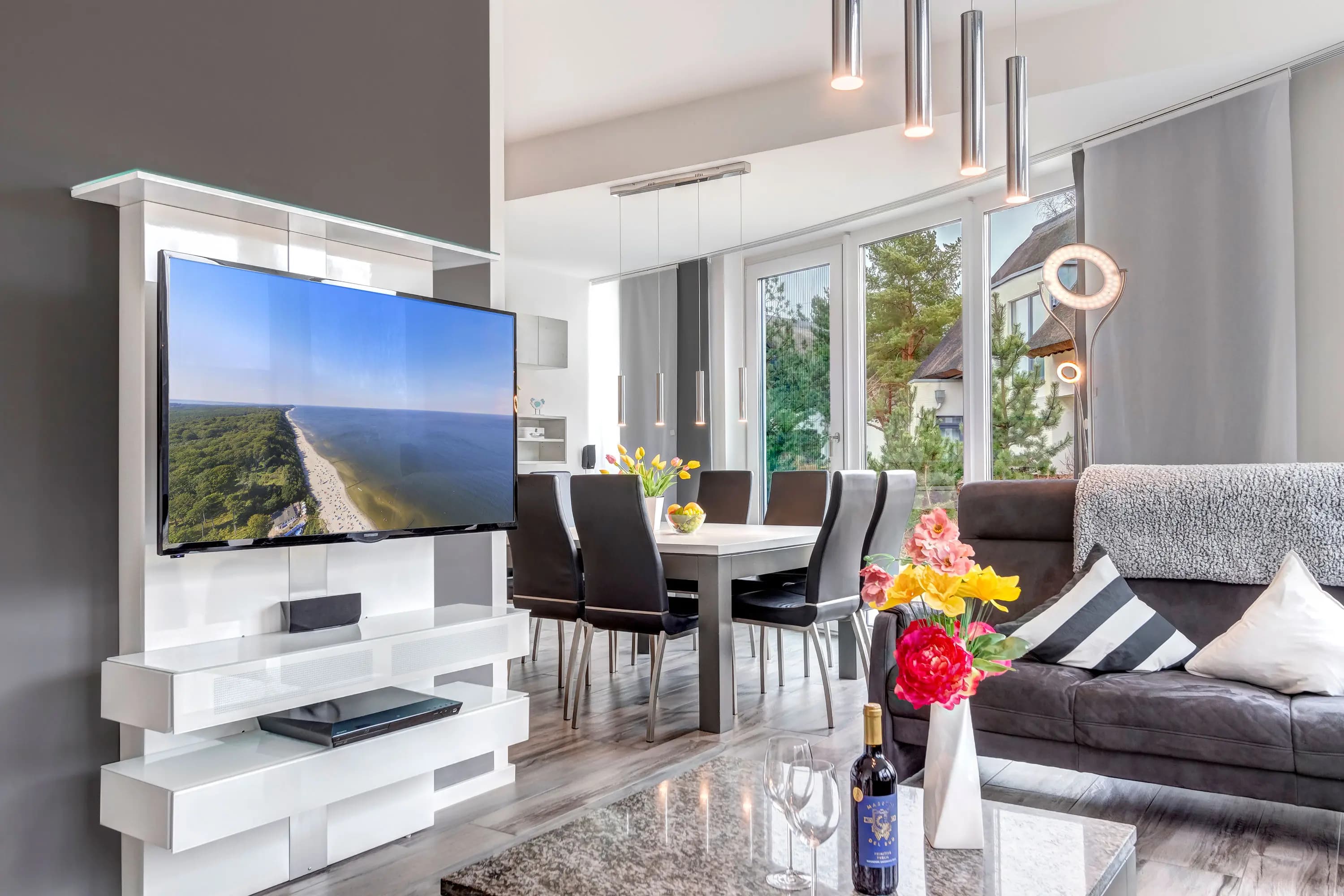 Offener Wohn- und Essbereich mit weißem TV-Möbel, Esstisch und großen Fensterfronten
