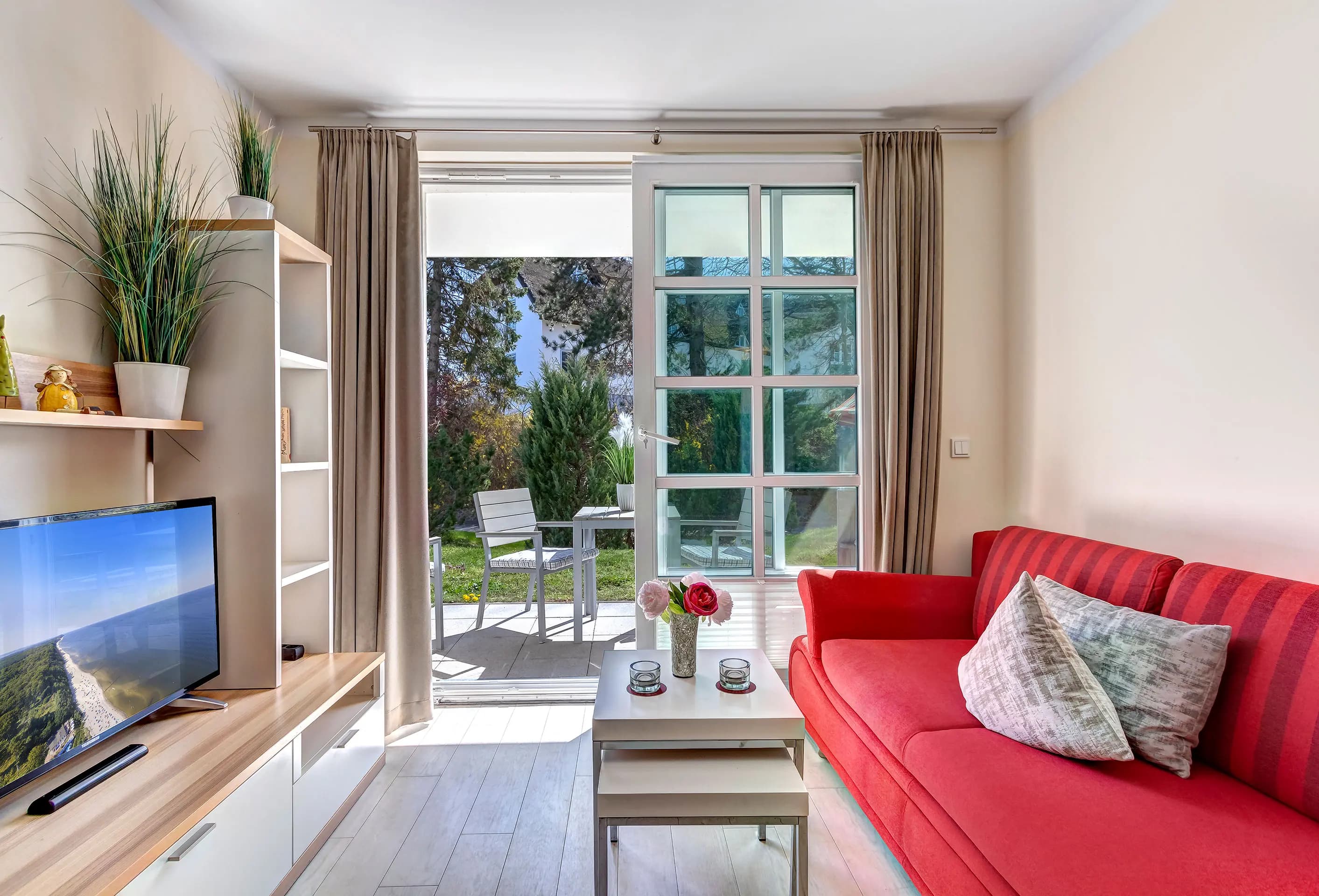 Wohnzimmer mit rotem Sofa und offener Terrassentür zum Garten